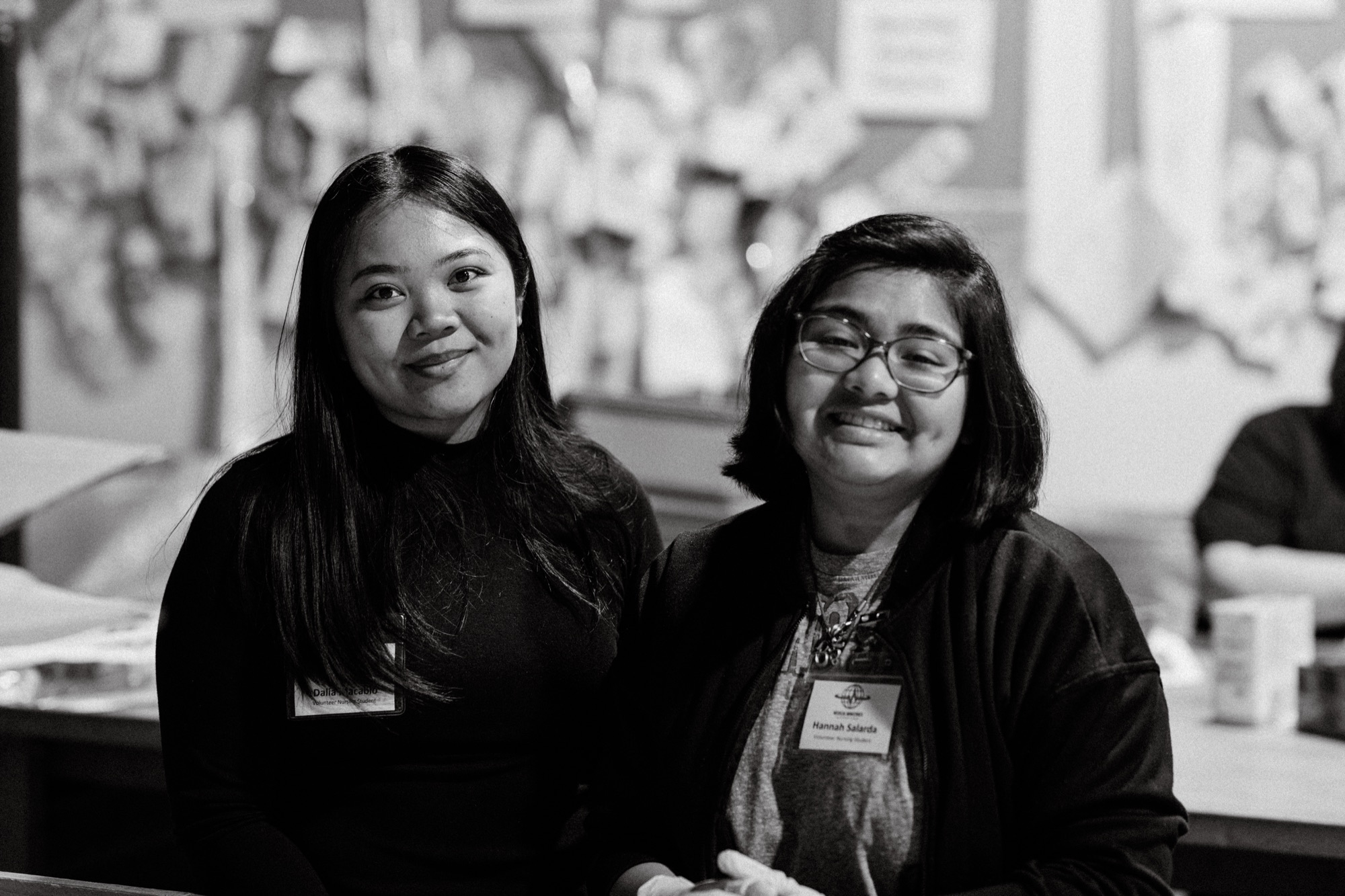 Two smiling student volunteers wearing name badges at the MMI warehouse
