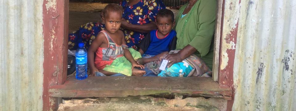 Two children and a local caregiver in a doorway in Fiji